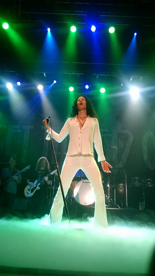 Paul Sinclair of Led Zeppelin tribute band, Get The Led Out on stage during one of the band's gigs. Blue and green stage lights beam down and stage fog is rolling in the foreground.