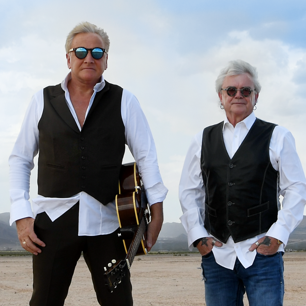 Russell Hitchcock and Graham Russell of Air Supply stand in the desert for an Air Supply promotional shoot. Graham Russell has a guitar under his arm.