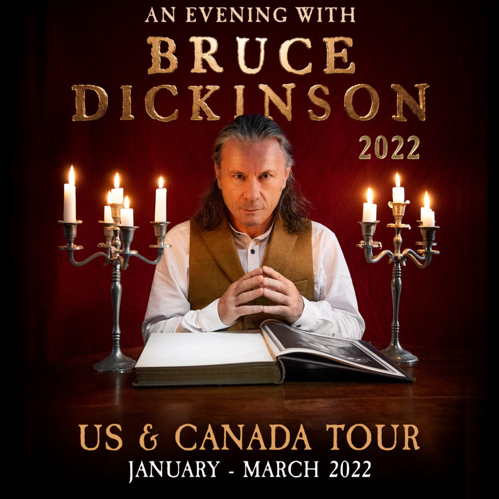 A promotional photo for "An Evening With Bruce Dickinson." Bruce Dickinson has candlesticks on either side and an opened book splayed out in front of him.