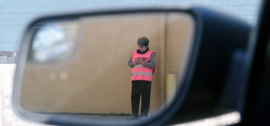 A clinic escort looks at their phone. The picture is a reflection of the photographers side mirror on their vehicle.