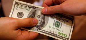 A person hands another person a 100 dollar bill