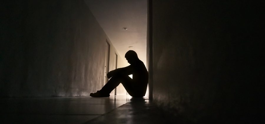 A person sits in a dark hall, their silhouette backlit