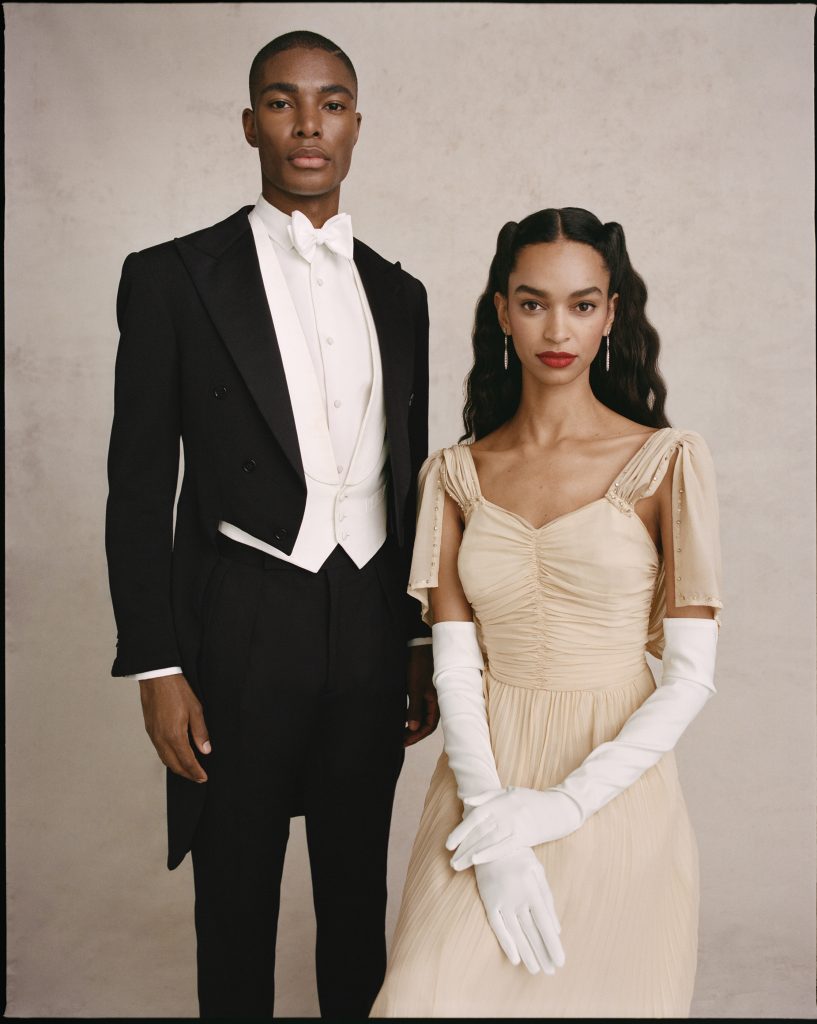 A Black man stands for a portrait in a fancy tuxedo while a Black woman sits in an elegant cream dress
