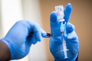 A Moderna COVID-19 vaccine is prepared during a pop-up vaccine clinic at Cristo Rey Church in East Austin. The photo shows two gloved hands holding an upside down syringe and vaccine dose
