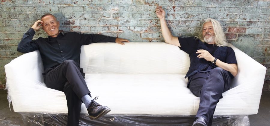 Curt Smith and Roland Orzabal of Tears for Fears pose on a white couch for a promotional photo.