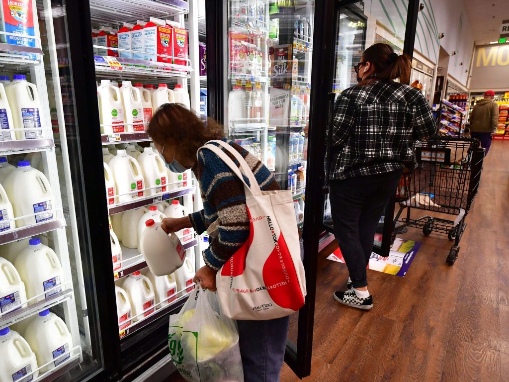 A person pulls out a gallon of milk as people shop at a grocery store