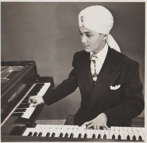 black and white of man in Indian turban playing two pianos