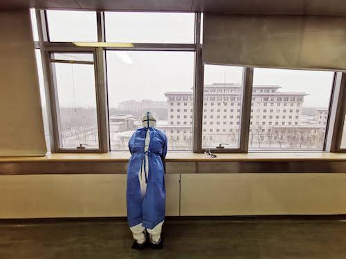 medical professional in protective gear looking out window in Wuhan