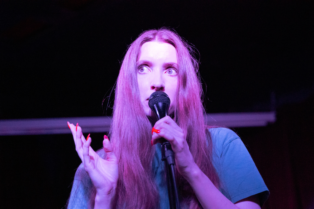 Florence Shaw of Dry Cleaning performing at Ace of Cups in Columbus, OH. Shaw is the vocalist of the group, and is holding a microphone in this image with a spotlight on her intense expression.