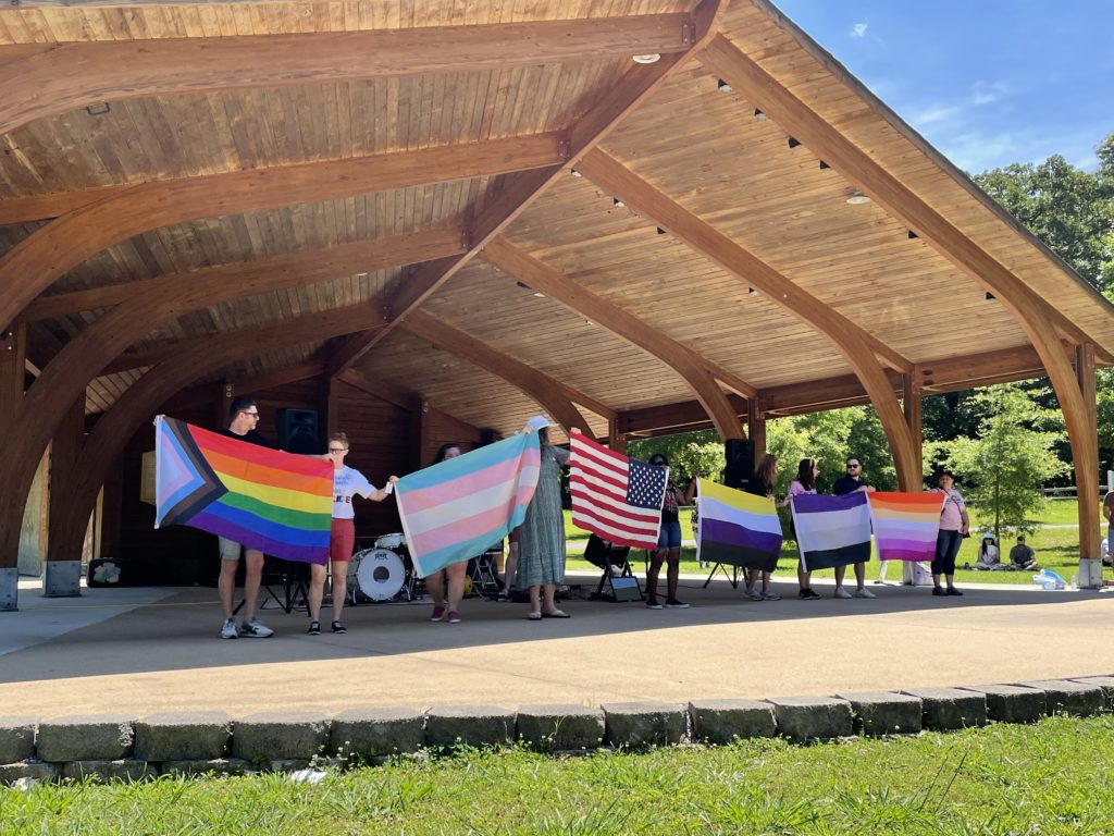 People hold Pride flags at an outdoor pavilion. 