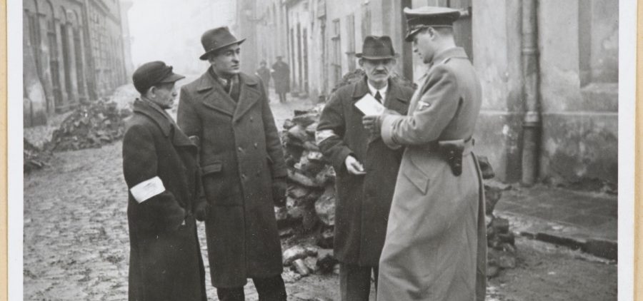 A German policeman checks the identification papers of Jewish people in the Krakow ghetto. Poland. Circa 1941.