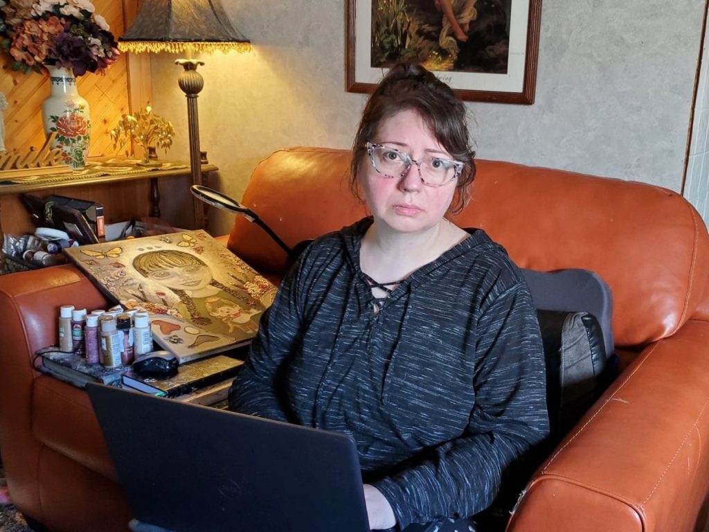 Georgia Linders sits on a couch with a laptop in her lap.