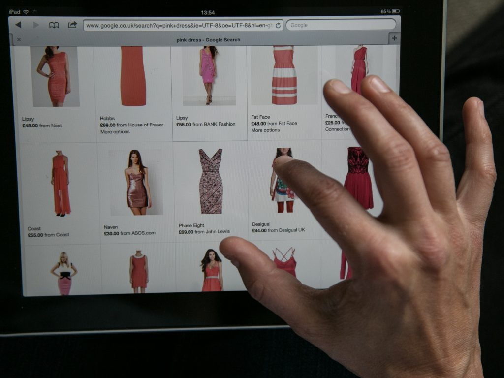 A person's hand is on a ipad looking at dresses.