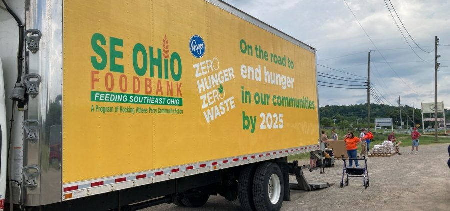A large truck with the logo of the Southeast Ohio Food Bank sits in front of a group of volunteers with food.