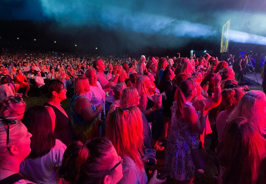 A large crowd of people gathered to see Rick Springfield perform at the 2022 Lancaster Festival. Rows of standing people are turned toward the stage. 