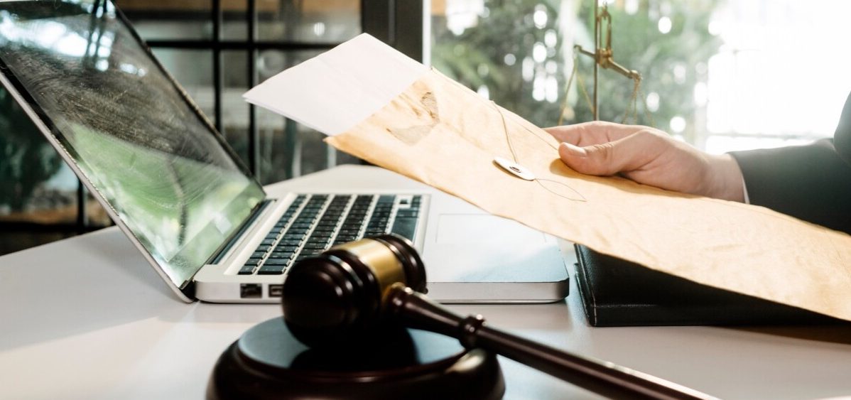 A person looks over a legal document and has a laptop and gavel on their desk.