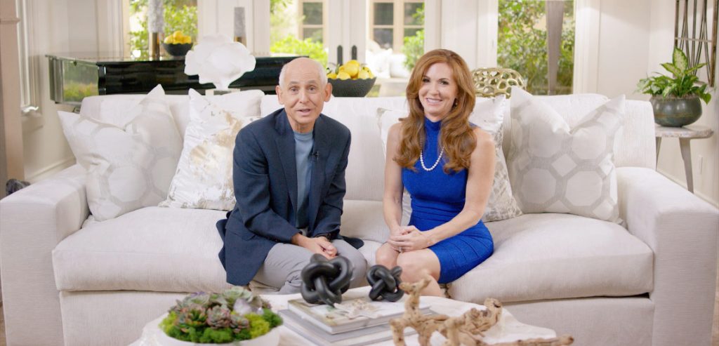 A promotional image for Dr. Daniel Amen's programming, and this image shows Dr. Daniel Amen sitting on a white couch with Tana Amen. They appear to be in a living room of some type.