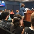 A city resident speaks to the Athens City Council. The photo is taken from the back of council chambers and there are residents filling almost every seat.