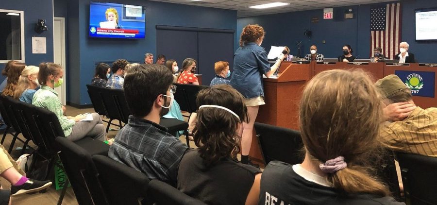A city resident speaks to the Athens City Council. The photo is taken from the back of council chambers and there are residents filling almost every seat.