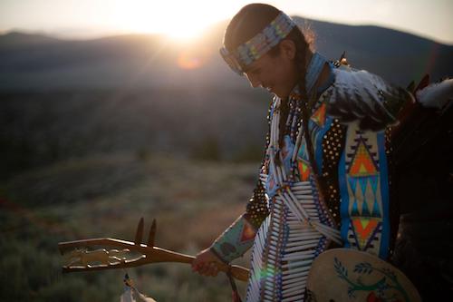 native american teen in full regalia with mountains and sunset in the background
