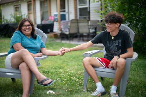 mother and teen son sitting outside on yard chairs holding hands