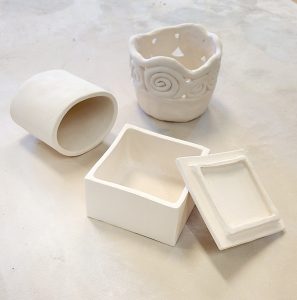Unpainted white clay pieces are clustered together. They are on a white tabletop.