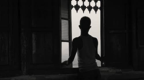 sillhouette of man looking out window with shutters