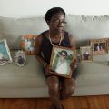 Black mom on couch surrounded by photos of son killed by hazing