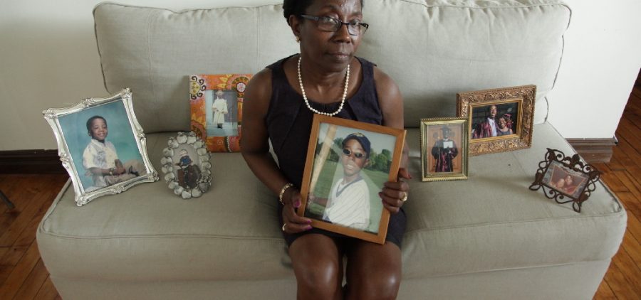 Black mom on couch surrounded by photos of son killed by hazing
