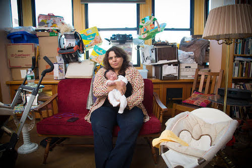 woman sitting in hoarded living room holding baby