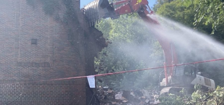 A backhoe demolishes the brick front wall of the former Trimble school building.