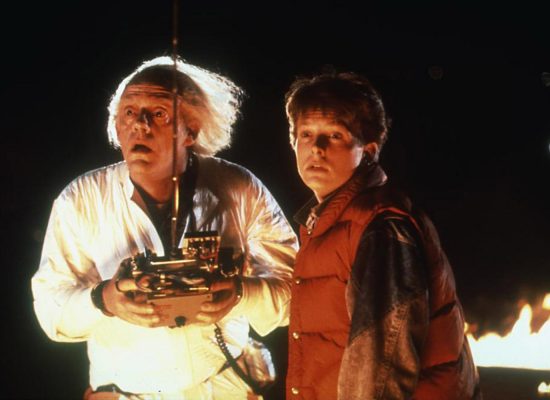 A still from the film "Back to the Future." Two male presenting men, one older and one younger, look in awe while holding a mysterious object.