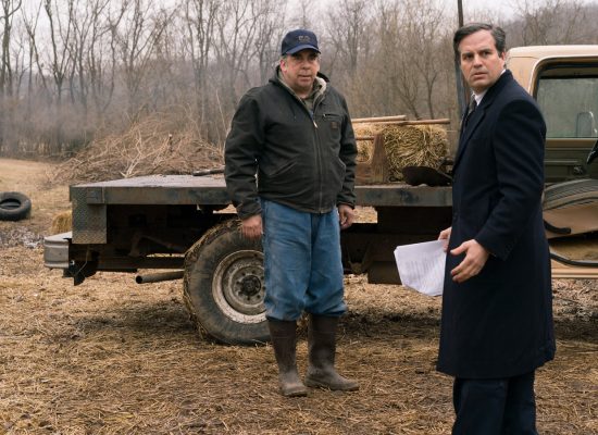 A still from the film "Dark Waters." Two male presenting people in winter clothes are standing outside of a pickup truck in a field.