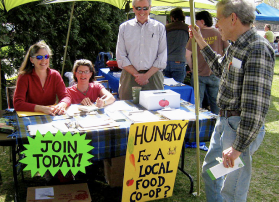 An image of five people assembled in what looks like a farmer's market type of arrangement with outdoor tents.