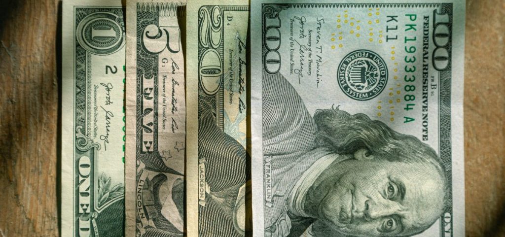 A one, five, twenty and one hundred dollar bills lined up next to each other.