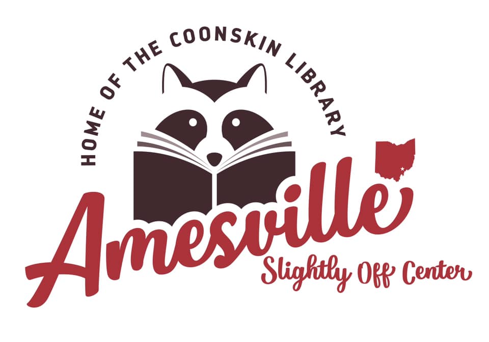 A logo with a raccoon reading a book in the center. The text of the logo reads Home of the coonskin library: Amesville - slightly off center.