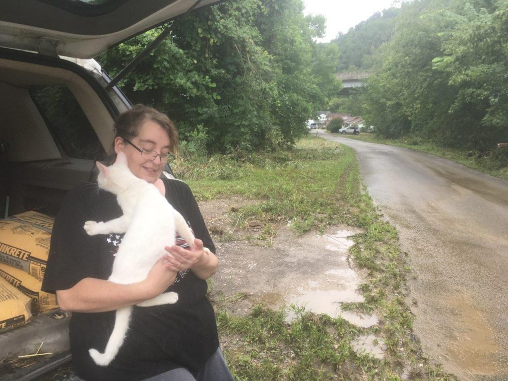 Pam Dawn holds a cat and leans up against the open trunk of an SUV