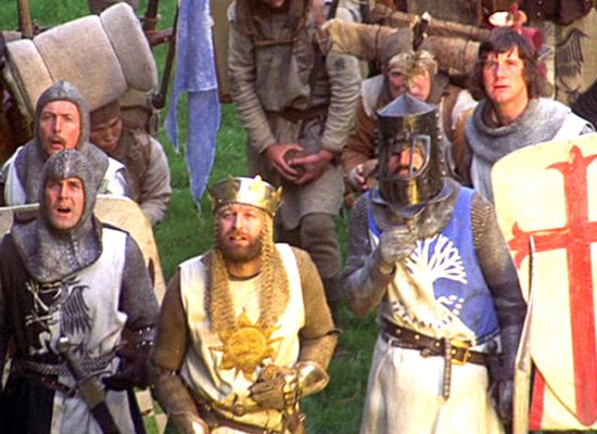 A still from the film "Monty Python and the Holy Grail." A number of people in medieval style costume clothing are gathered together.