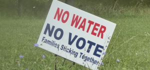 A sign reads No Water No Vote: Families Sticking Together