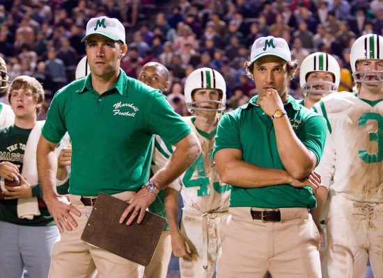 An image of Marshall University football players and officials. The officials are in the foreground of the picture, and they are wearing green polos.