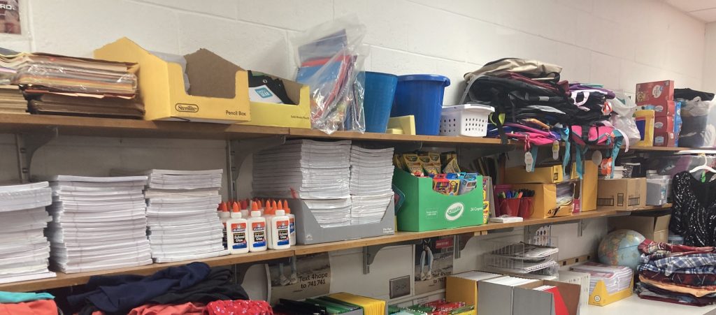 Shelves full of paper, glue, clothes, and other school supplies.