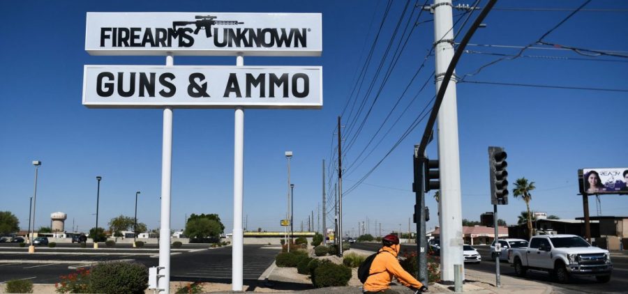 A person rides a bike in from of a sign for a firearms unknown guns and ammo store