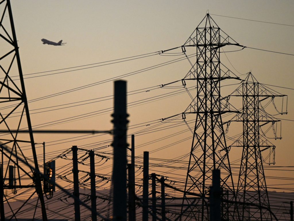 An aircraft takes off from Los Angeles International Airport (LAX), with electric power lines visible at sunset 