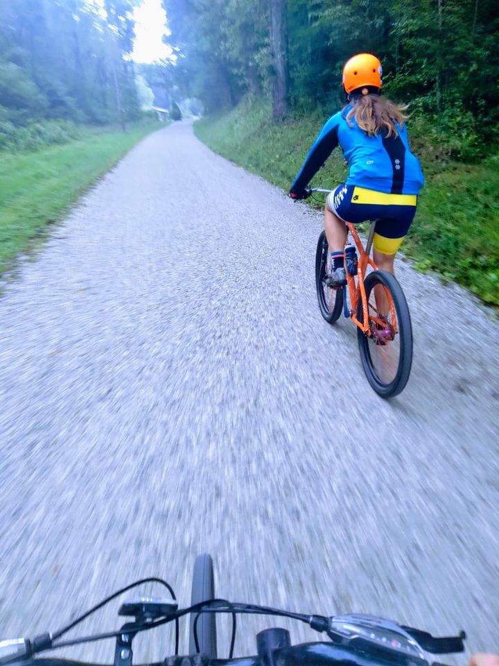 A person in a helmet rides their bike on the bike path surrounded by woods.