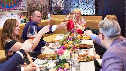 Chef Lidia at dining table with 5 others toasting across table