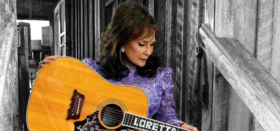 Loretta Lynnin purple dress holding guitar in barn