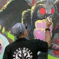 A man works on a mural of the Mothman.