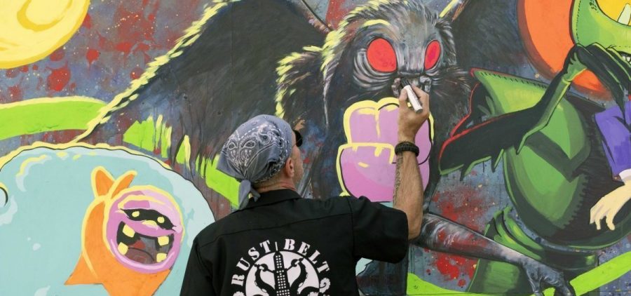 A man works on a mural of the Mothman.