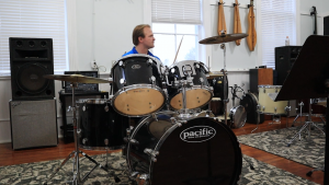 A volunteer, Brendan Hart, playing the drums that are available in the music lending library. 
