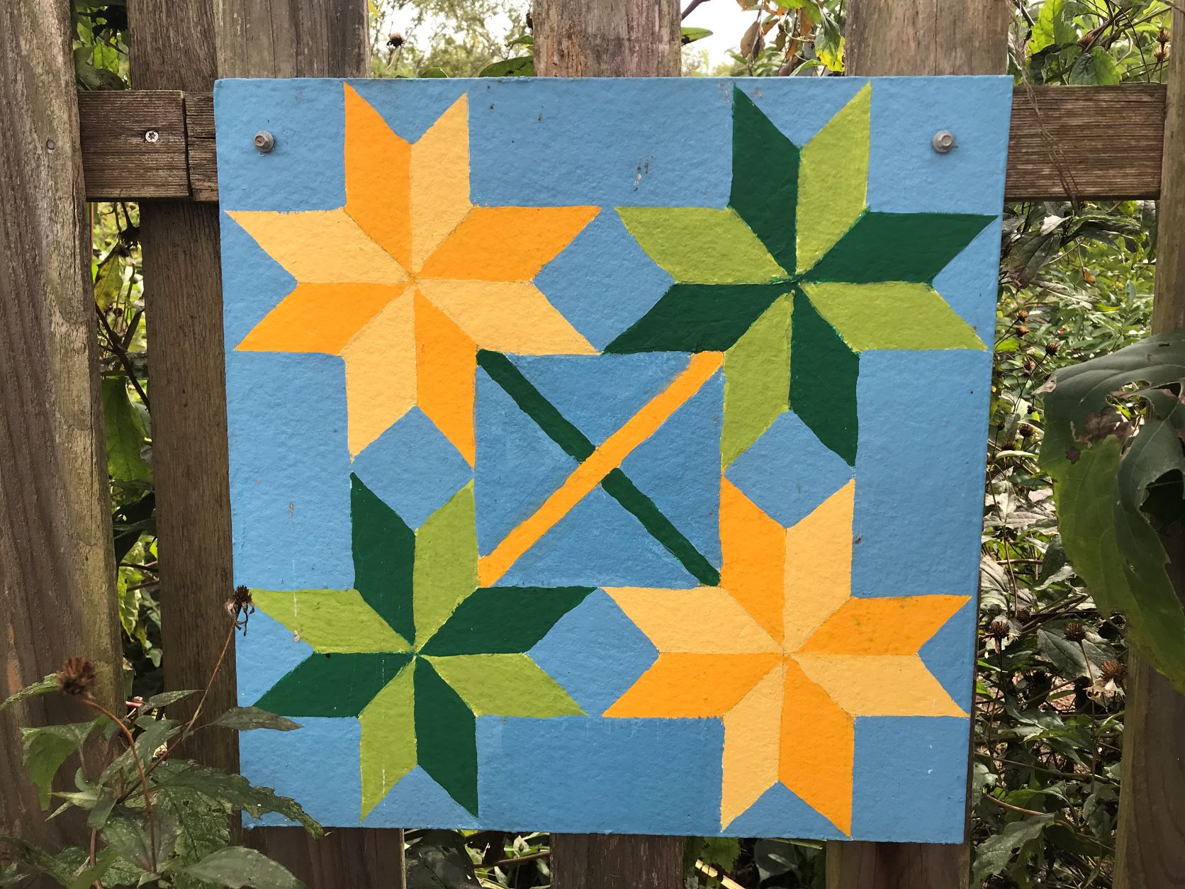 A picture of a quilt hung in the woods.